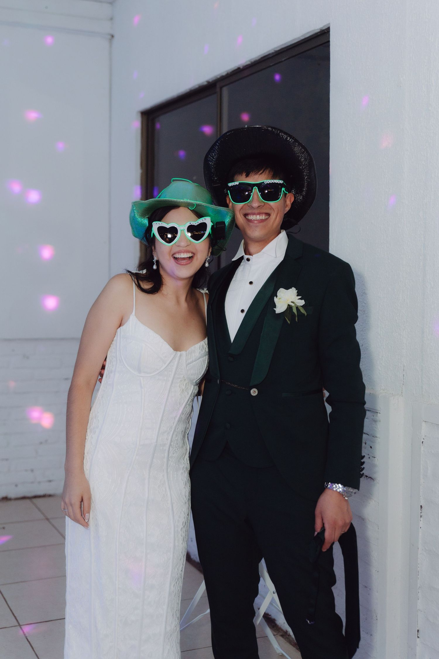 Bride and groom posing playfully with novelty sunglasses and hats at their wedding reception.