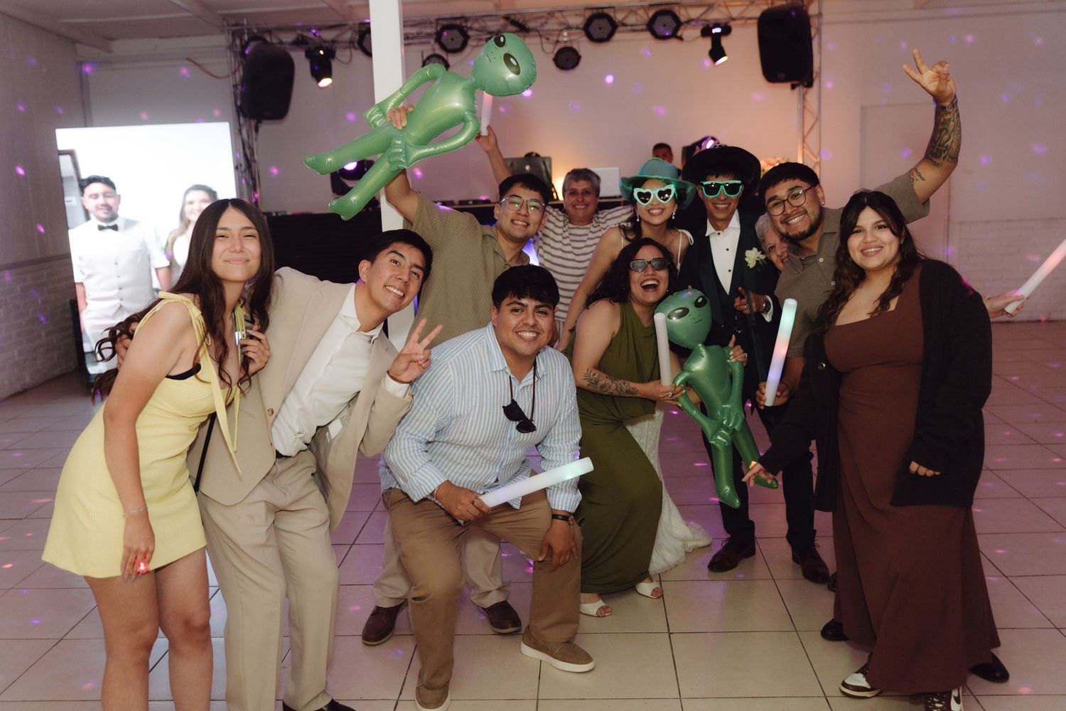 Group of wedding guests posing with inflatable alien toys and fun accessories at reception.