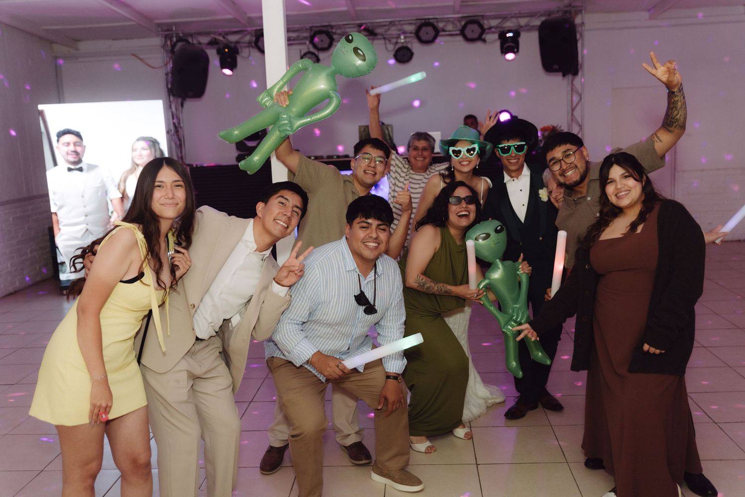 Cheerful group of wedding guests holding inflatable aliens and accessories at a lively reception.