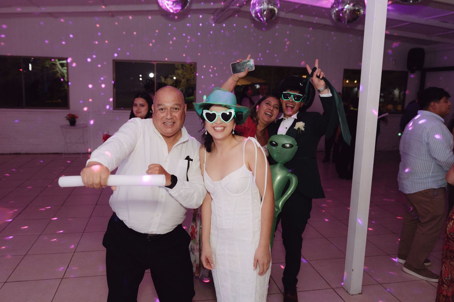 Bride in white dress and guest with glow stick dance at festive wedding reception party.