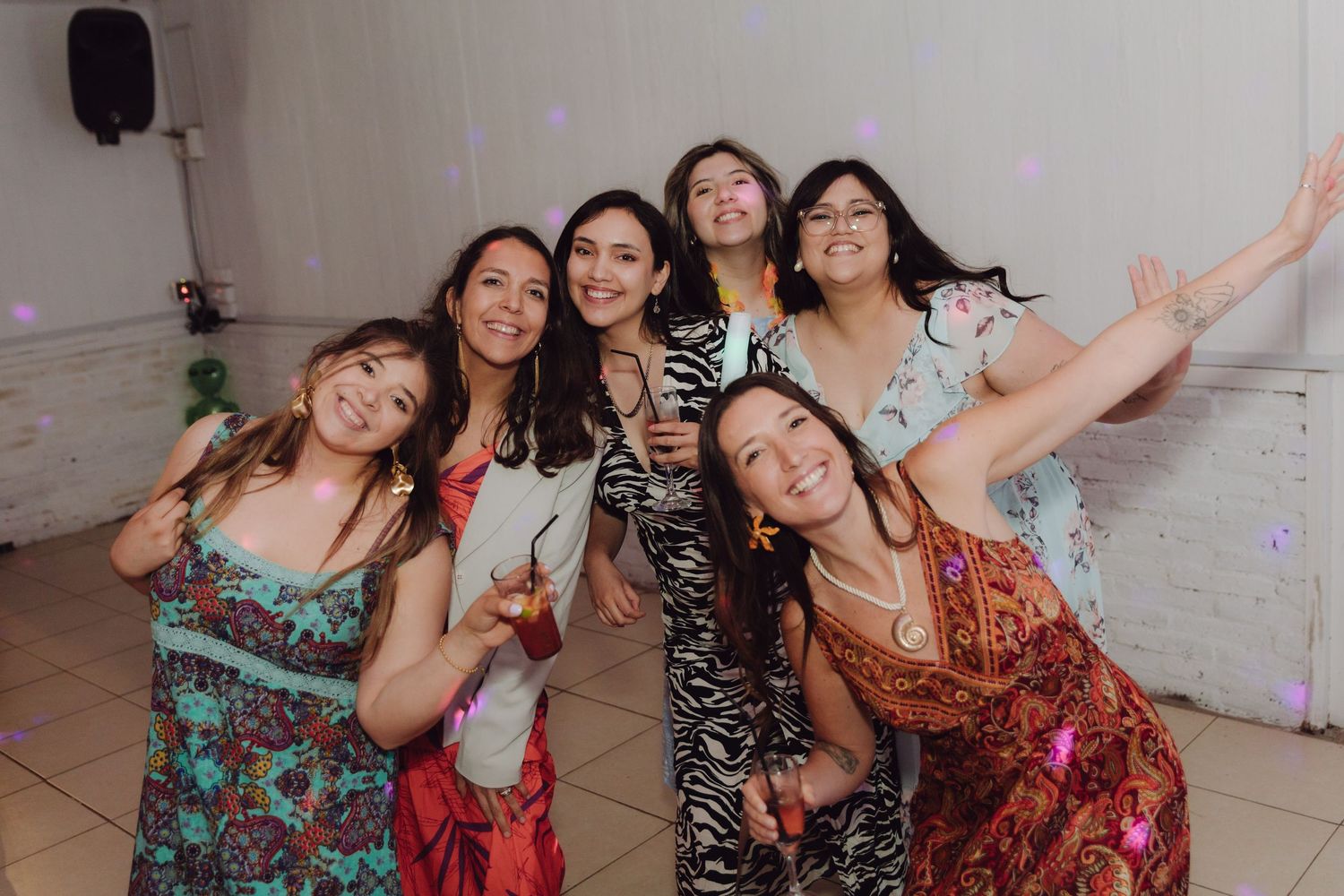 Group of seven women in colorful dresses smile and pose together at wedding reception.