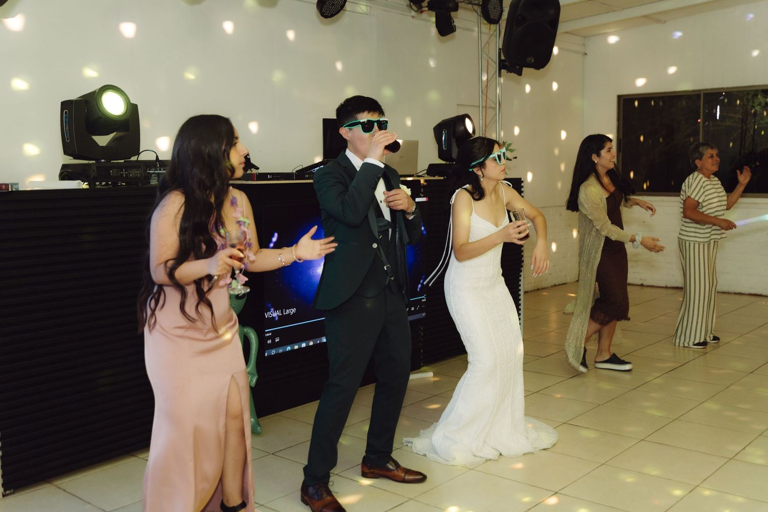 Bride groom and guests singing and dancing together near DJ booth at wedding reception.