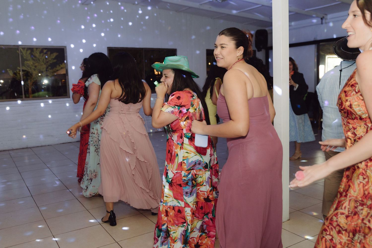 Wedding guests in colorful dresses dancing and celebrating on the dance floor at reception.