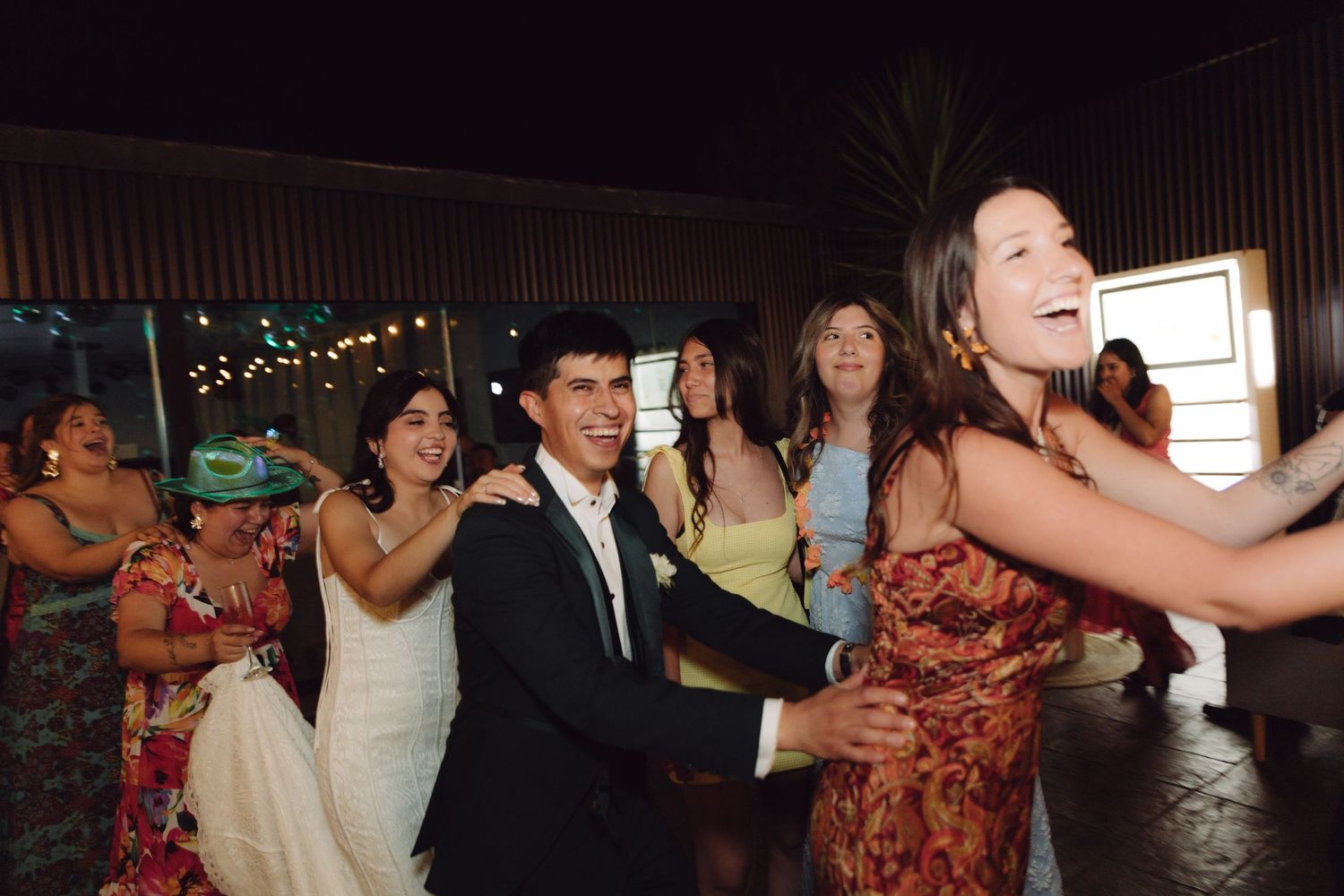 Bride groom and guests laughing and dancing together at outdoor wedding reception celebration.