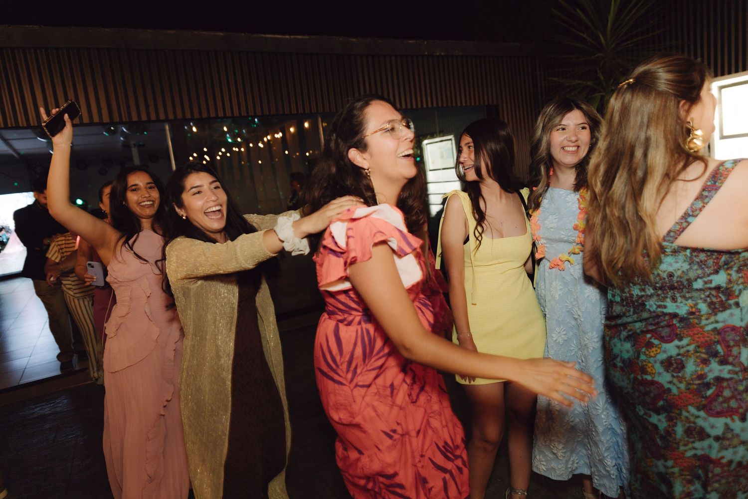 Group of women in elegant dresses laughing and dancing together at wedding reception party.