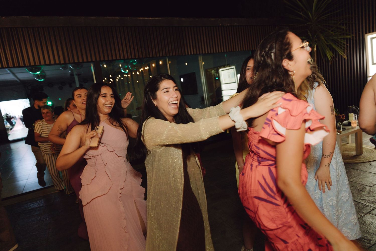 Excited wedding guests in pink and coral dresses dancing and celebrating at reception party.