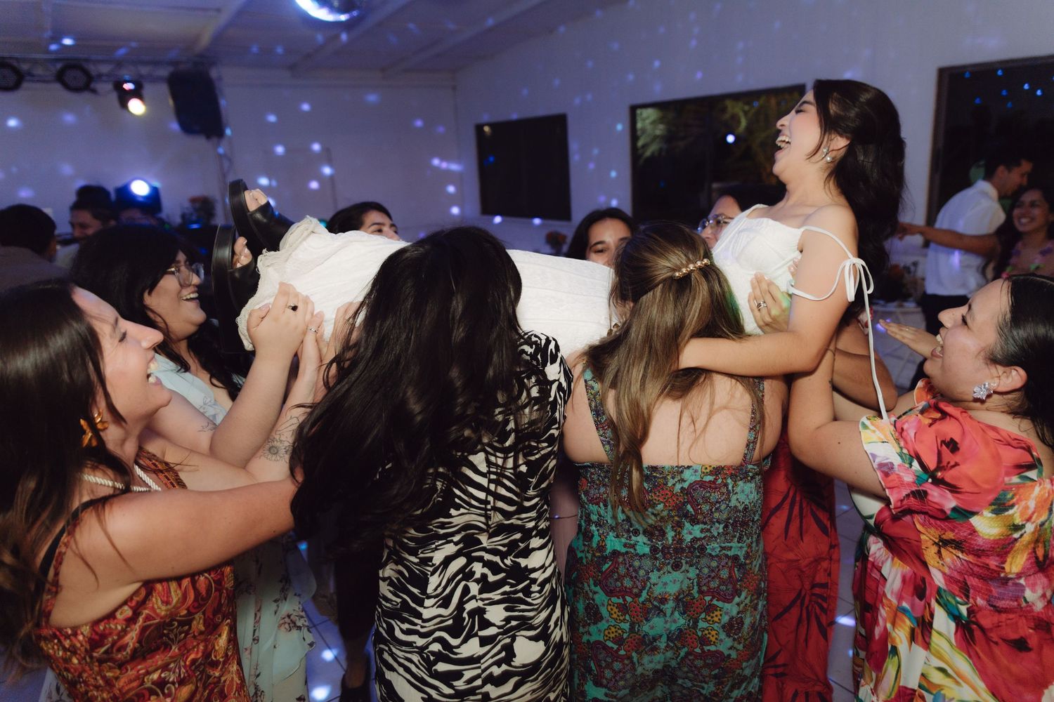 Joyful wedding guests lifting the bride in her white dress on the dance floor during the reception celebration.