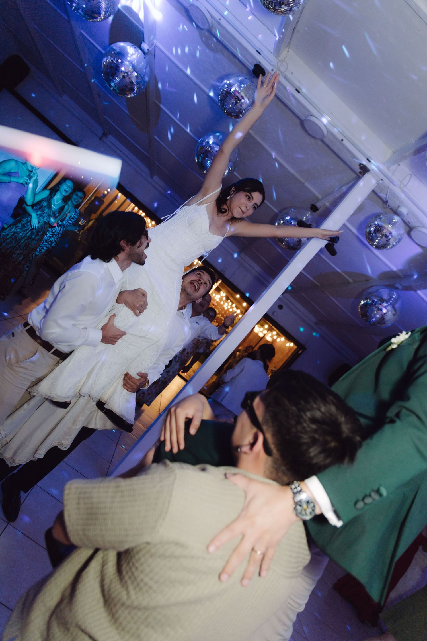 Bride in white wedding dress dancing under disco balls with guests at a vibrant wedding reception dance floor.