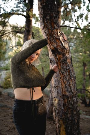 Moody forest portrait with cropped sweater against textured pine tree bark.