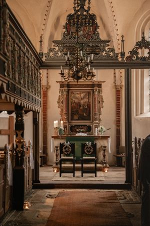 Zwei festlich geschmückte Stühle stehen vor einem kunstvoll verzierten Altar mit Kronleuchter in einer historischen Kirche.