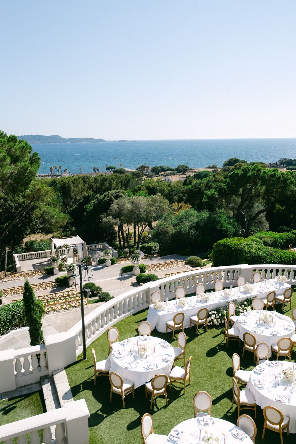 Elegant outdoor wedding reception on a terrace with white-draped tables, gold chairs, and stunning Mediterranean sea views.