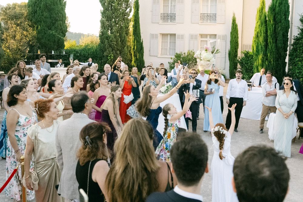 Elegant outdoor wedding celebration with guests cheering as bride and groom walk through crowd at a French villa.