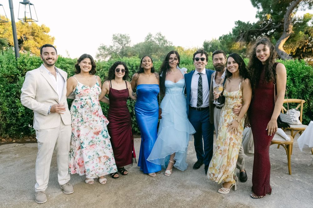 Group of elegantly dressed guests posing together outdoors at a wedding celebration in a garden setting.