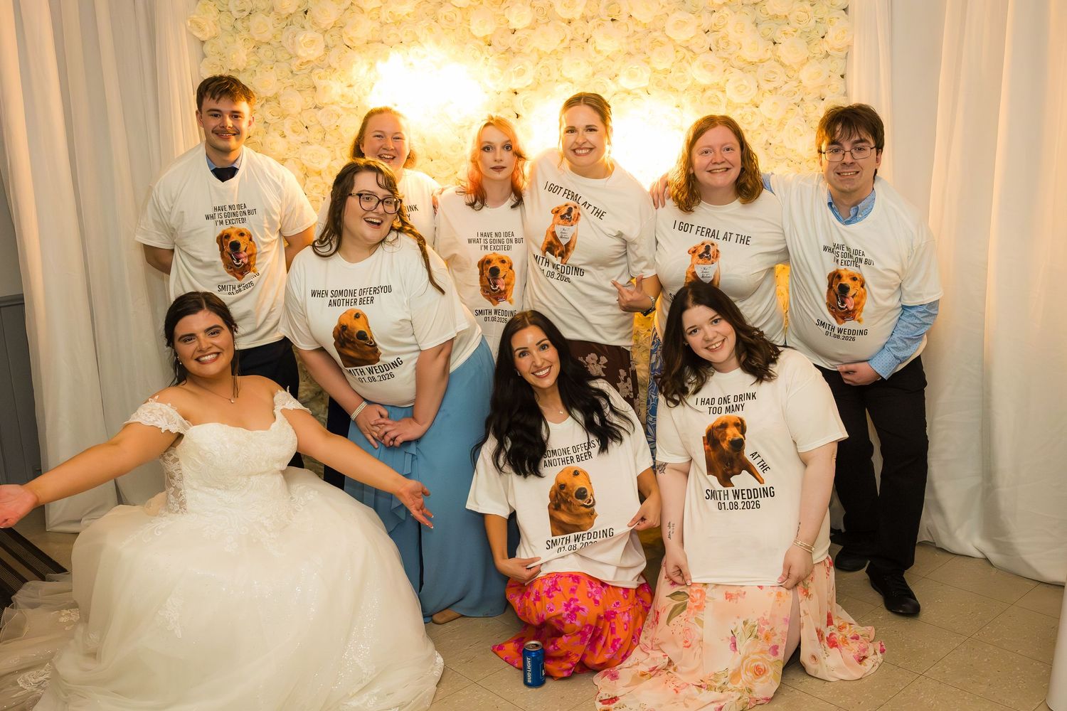 Bride in white gown poses with group wearing matching bear graphic t-shirts at a wedding celebration indoors.