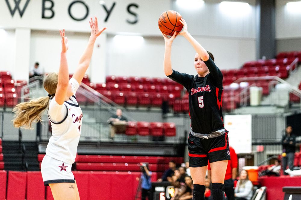 Player number 5 shoots a jump shot over defender in a girls basketball game.