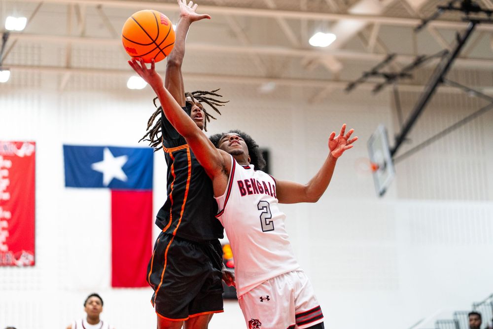 A basketball player in orange drives to the basket against a defender wearing number 2 in a Texas high school game.