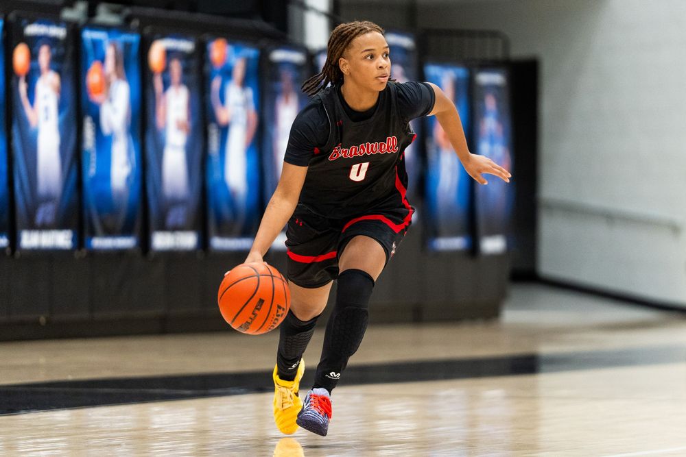 A female basketball player in a red uniform dribbles the ball during an indoor high school basketball game.