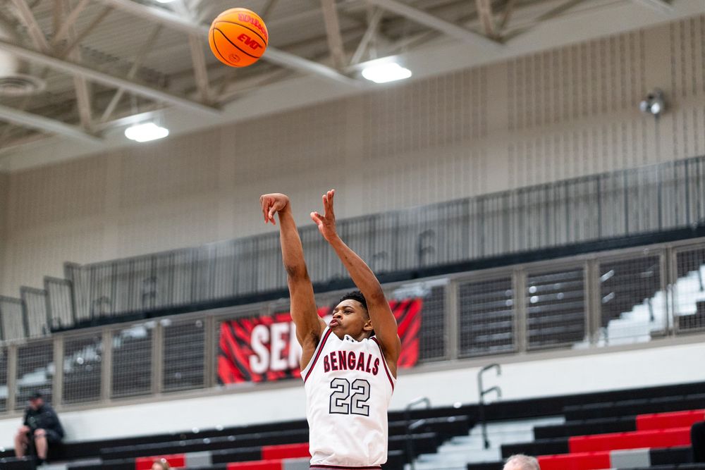 A Bengals player wearing number 22 shoots a jump shot in a white uniform during a high school basketball game.