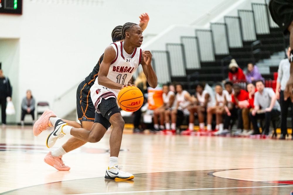 A Bengals player dribbles the ball in a white uniform during a high school basketball game.