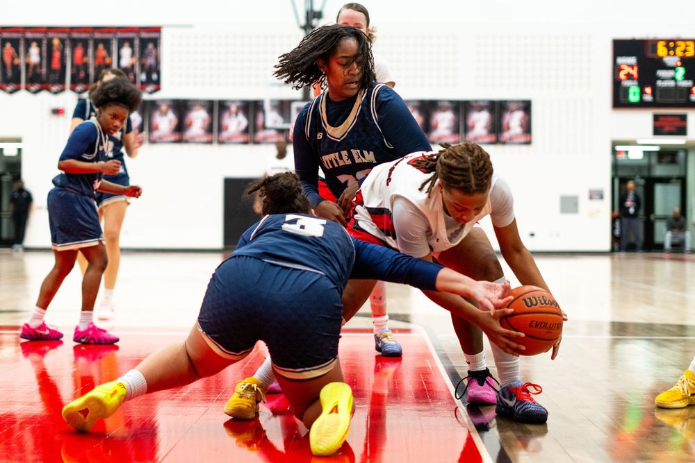 Two players battle for a loose ball on the court during a competitive high school girls basketball game.