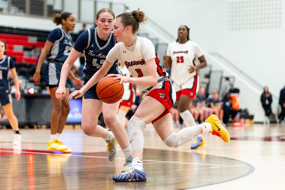 Female basketball player in red uniform drives past defender during indoor game.