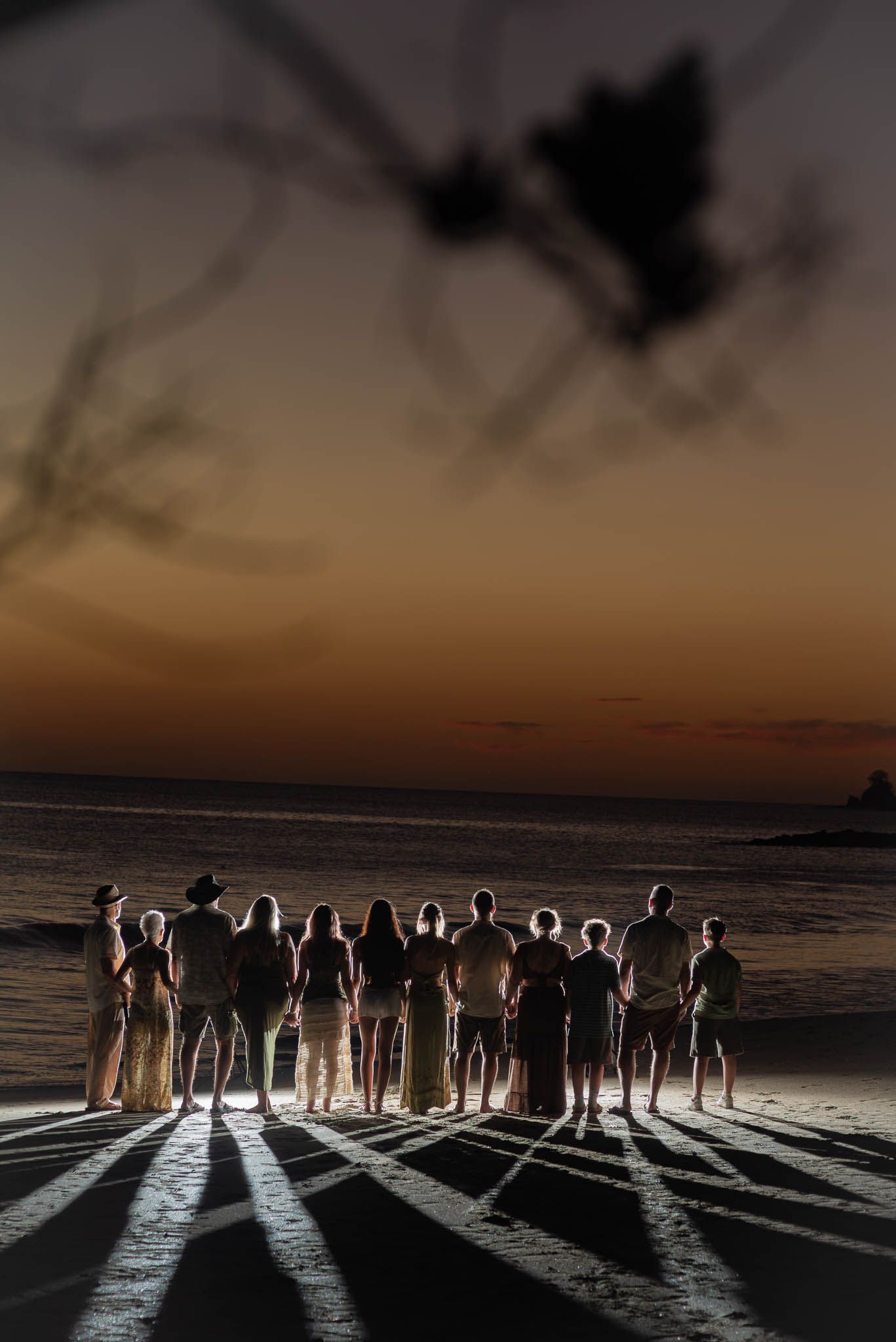 Silhouettes of a group of people standing together on a beach at sunset with dramatic shadows at Riu, Costa Rica