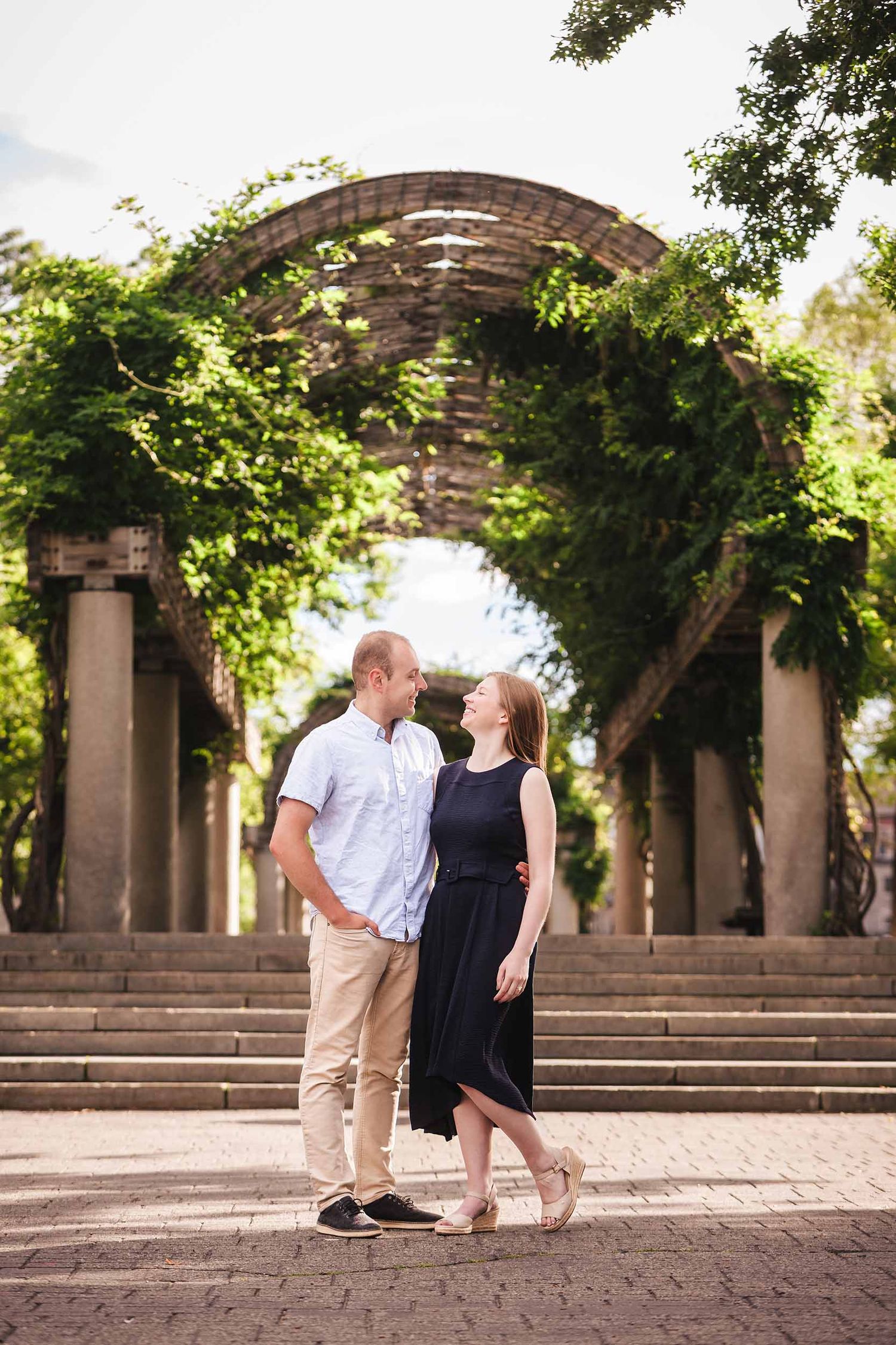 Engaged couple standing under the wisteria-covered wooden trellis at Christopher Columbus Park in Boston