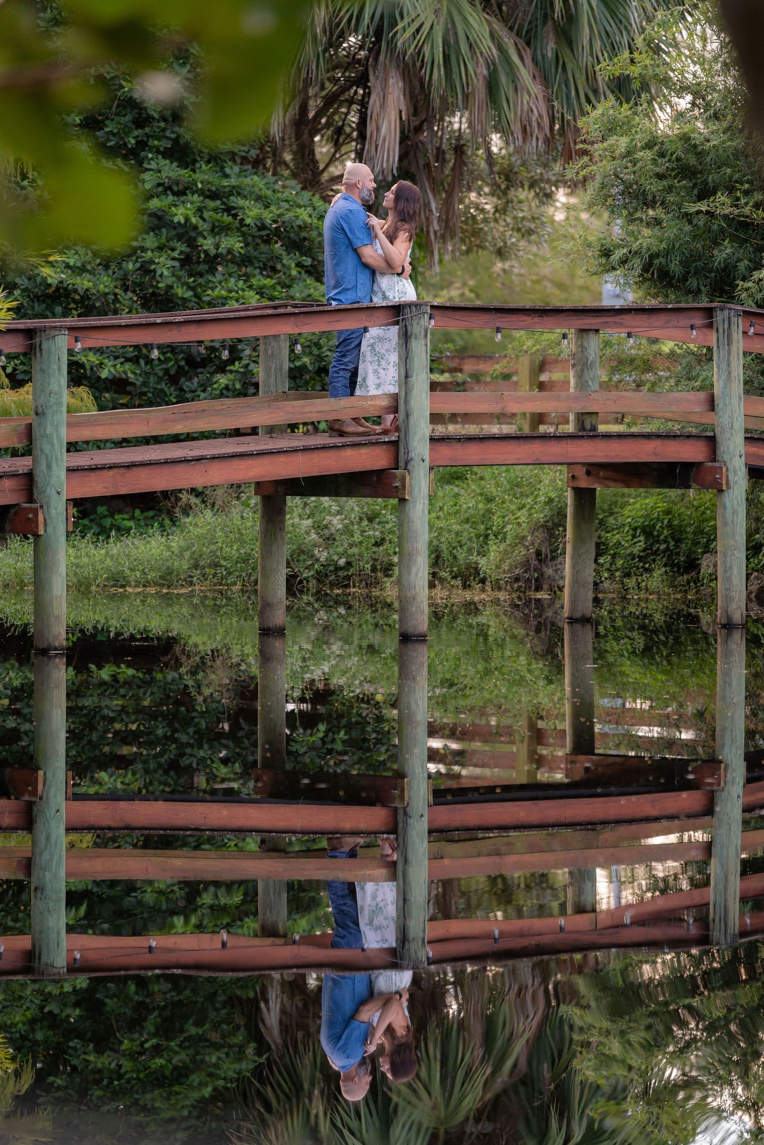 Couple embracing on the bridge over the pond with a mirror reflection at Rockin' H Ranch in Palm City, FL