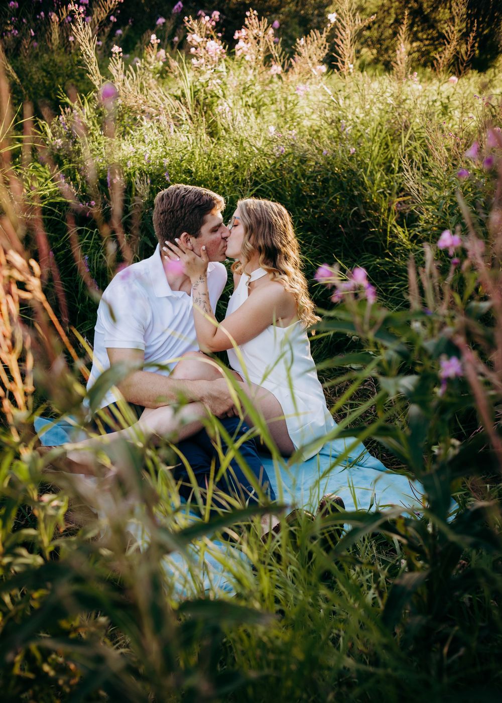 Couple sitting together in a field of tall grass and wildflowers during an outdoor portrait session