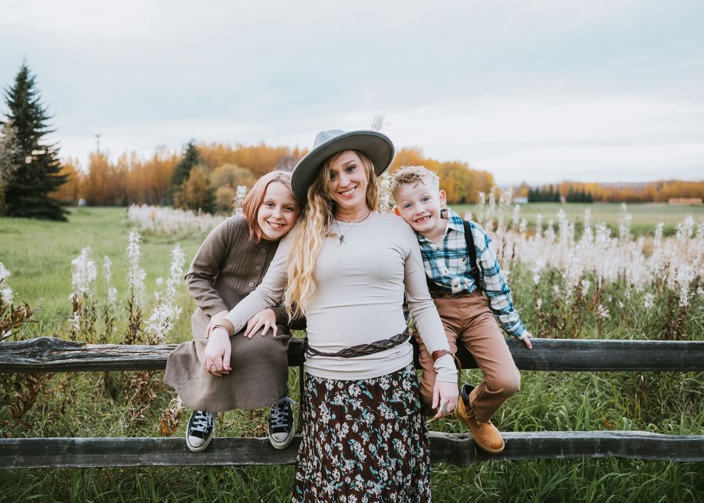 Mother standing with her two children outdoors beside a wooden fence during a family photography session