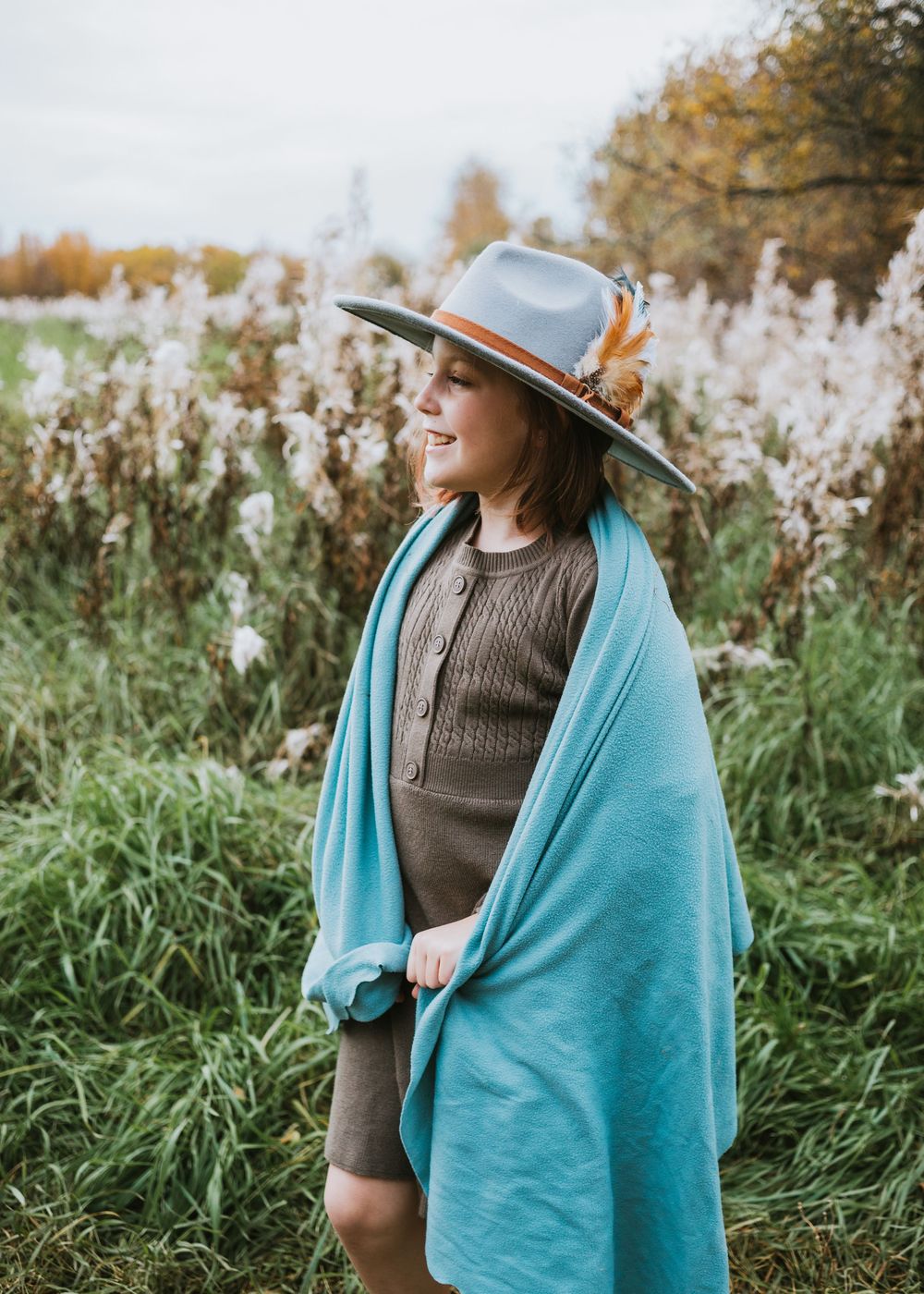 Little girl wearing a hat and wrapped in a blue shawl while standing in a field of wildflowers