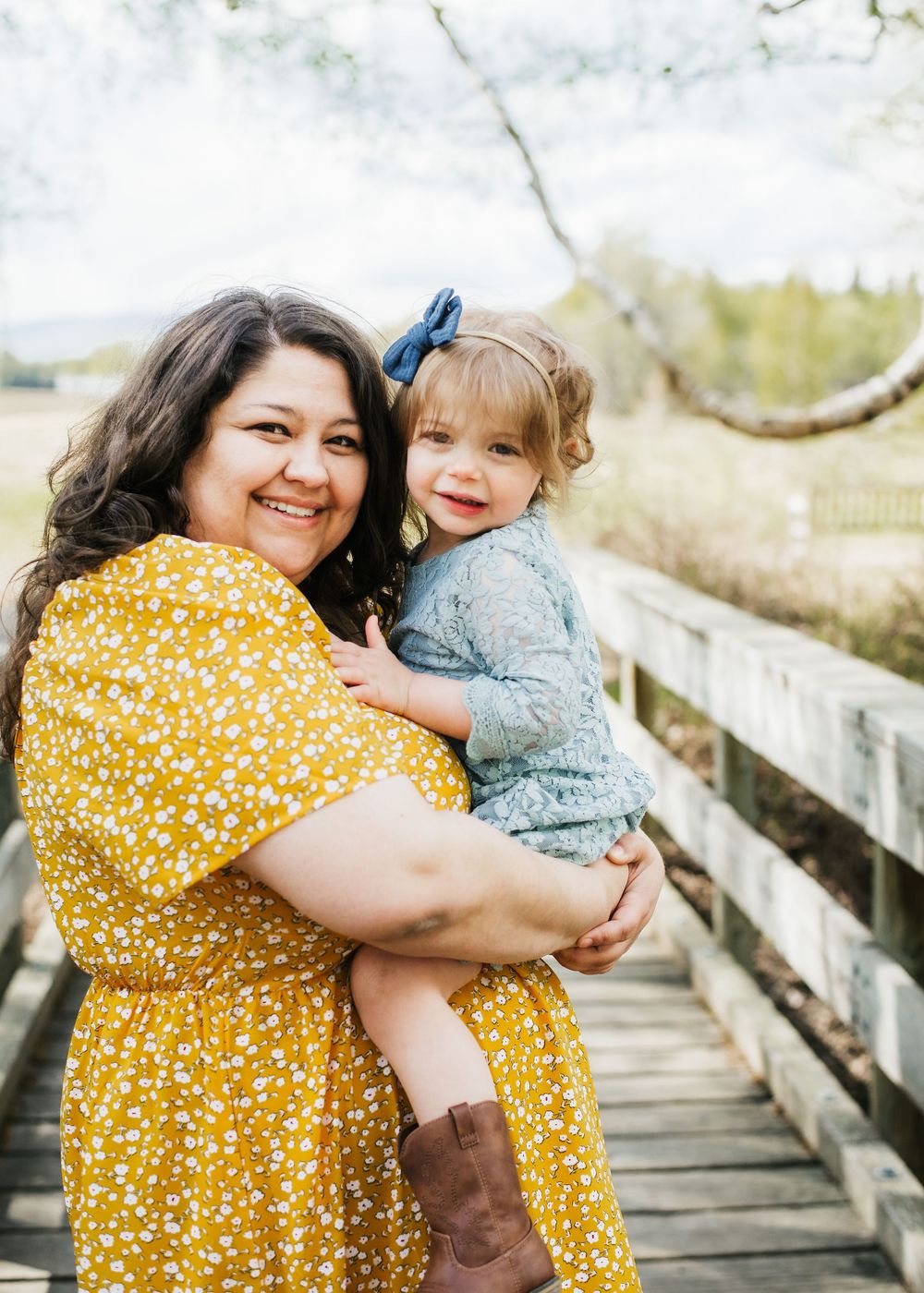 Mother holding her young child while standing on a wooden bridge during an outdoor family session
