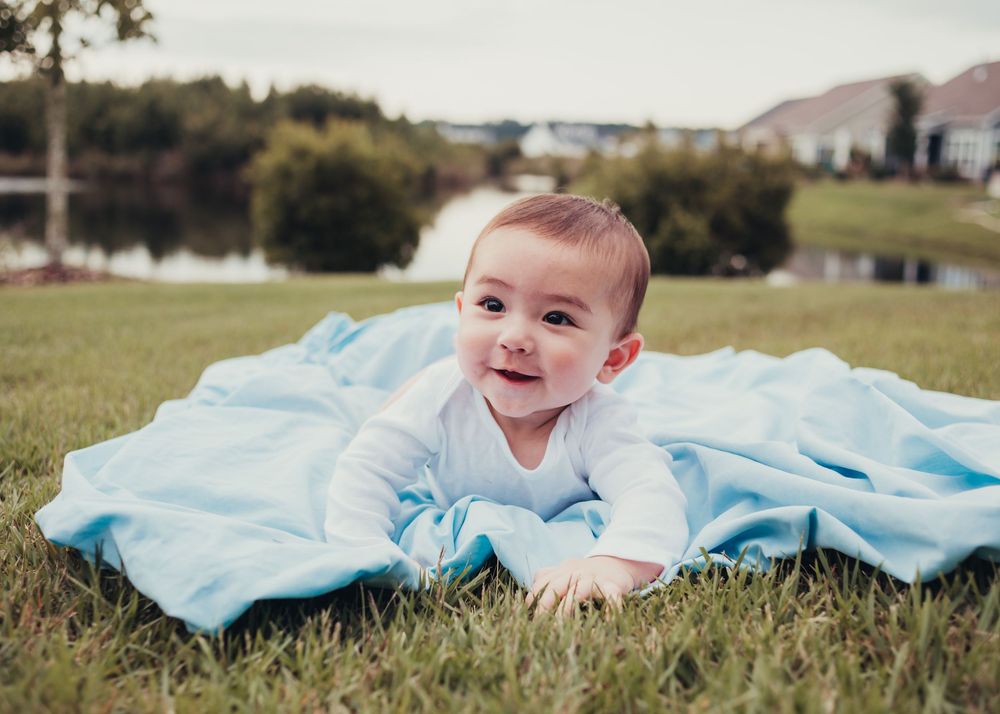 Smiling baby lying on a blue blanket in a grassy field during an outdoor portrait session