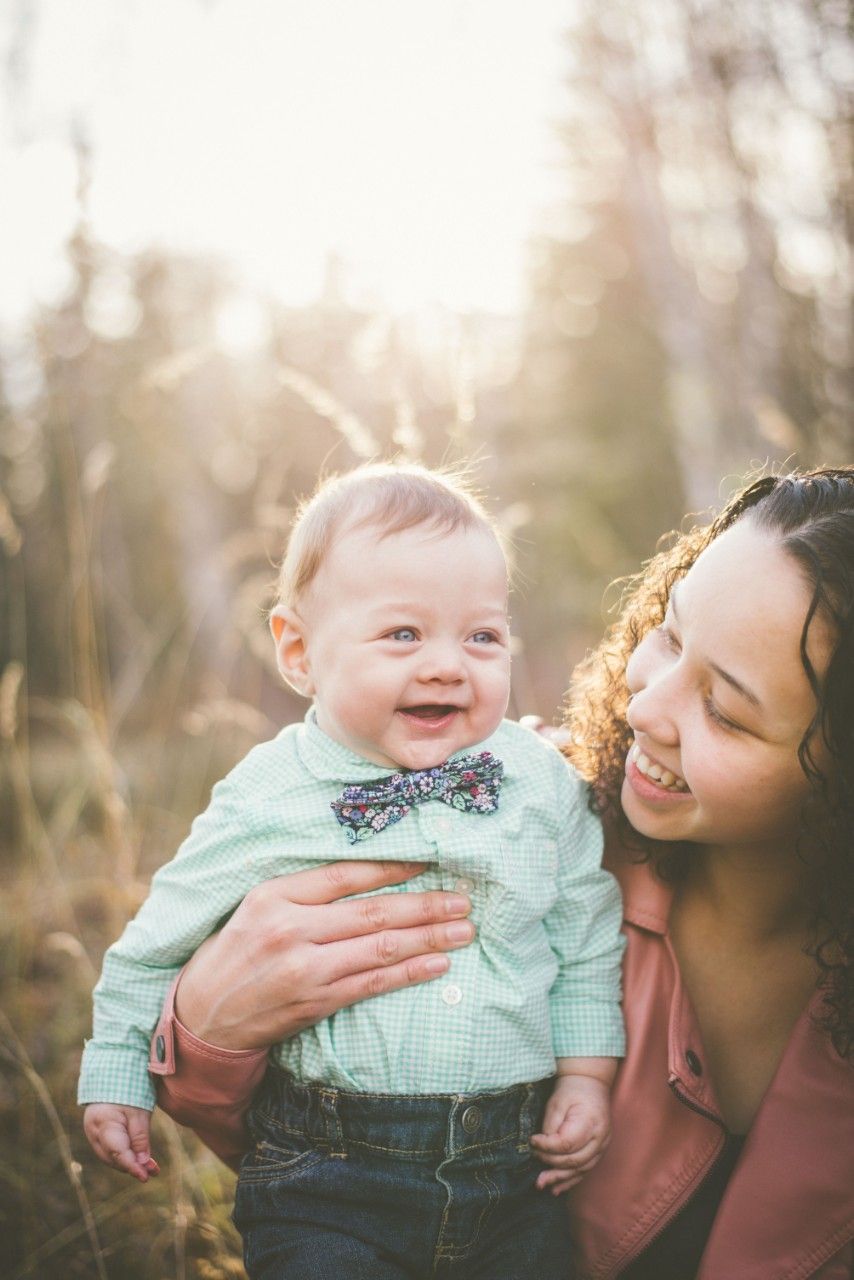Mother holding her smiling baby outdoors in warm evening sunlight during a family session