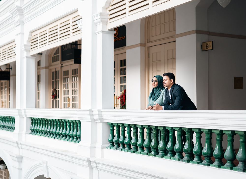 A couple in formal attire stand on a white colonial building balcony with green railings.