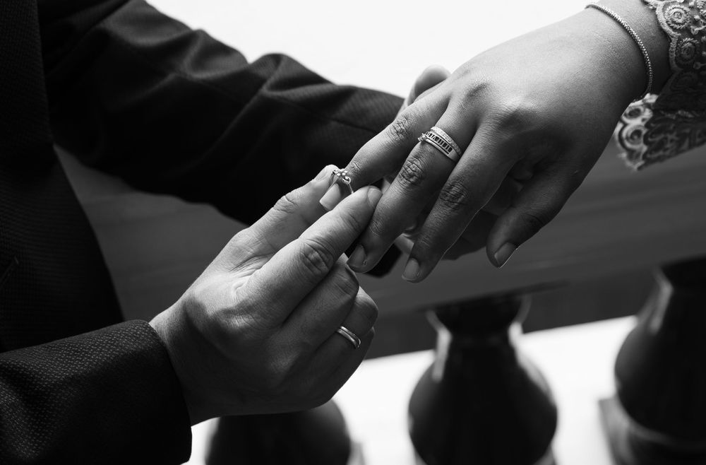 Black and white photo of a couple exchanging wedding rings during a romantic marriage ceremony proposal.