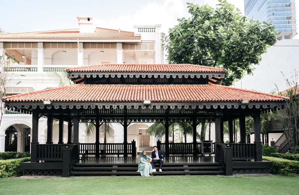 Couple poses under elegant black gazebo with red tile roof on manicured lawn at outdoor wedding venue.