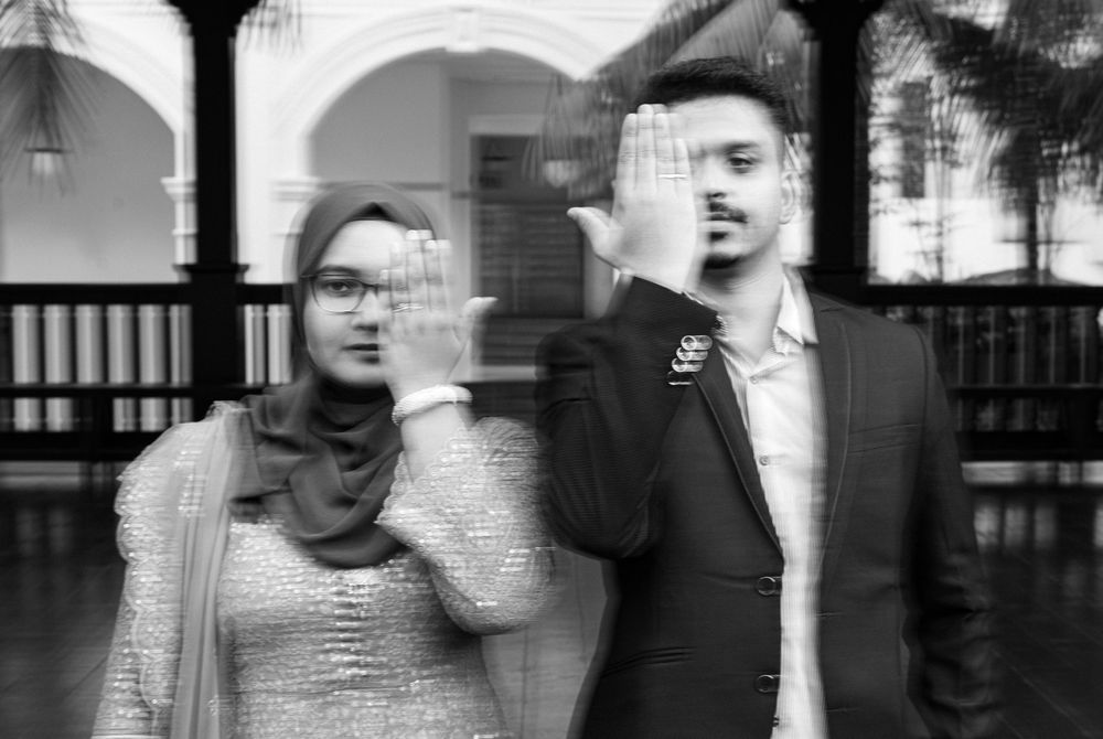 Black and white photo of a man and woman raising hands to cover faces in a blurred motion effect.