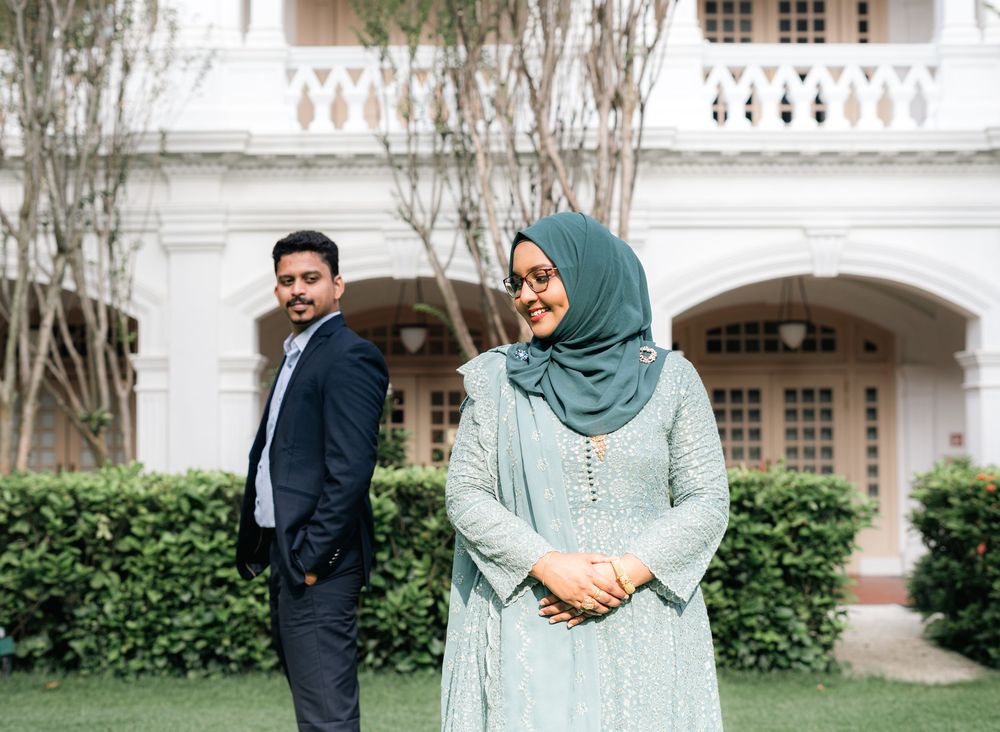 A man in a suit and woman in a mint green hijab and dress pose outdoors near a white colonial building.