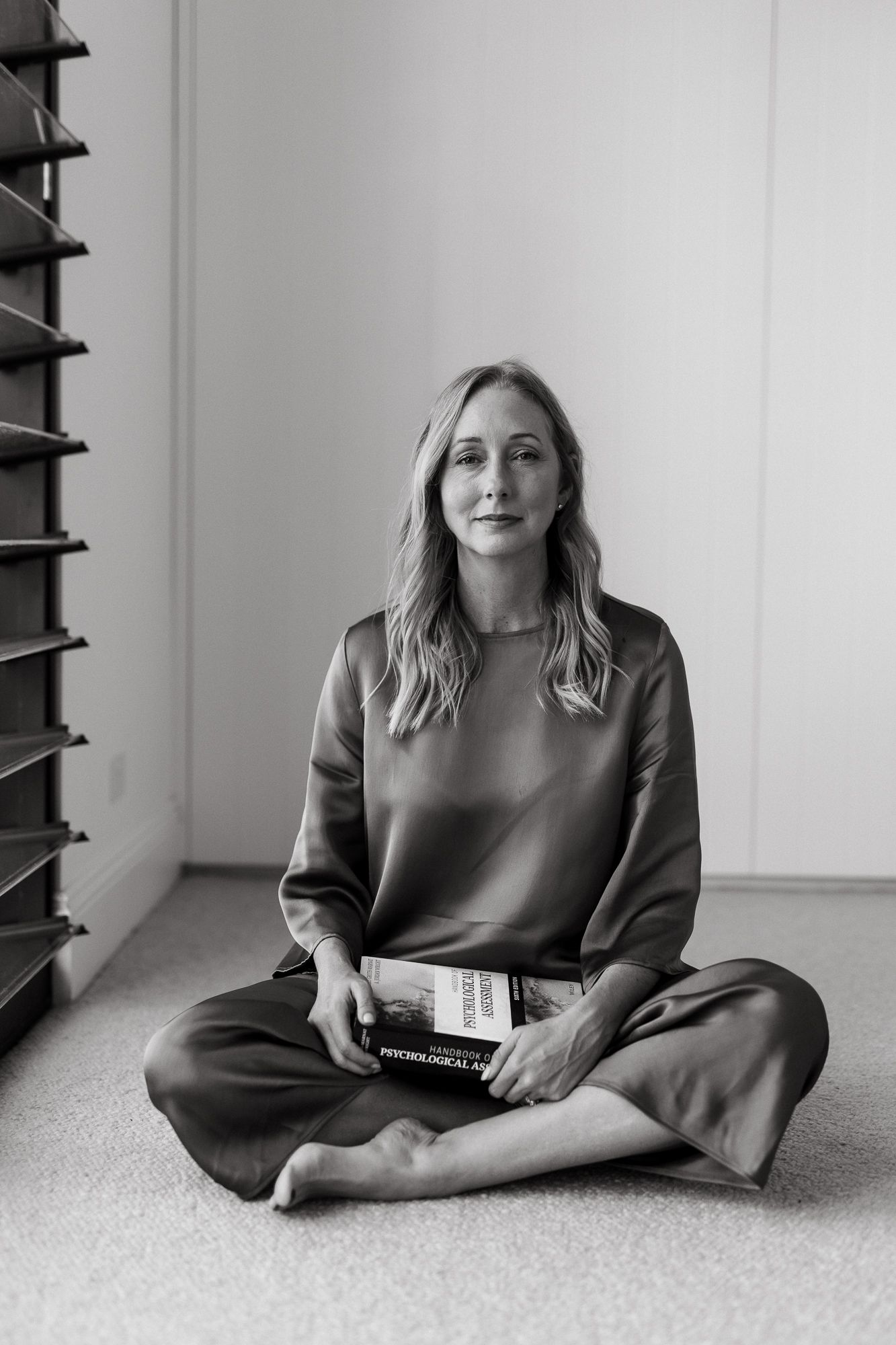 Black and white photo of a woman sitting cross-legged on floor holding a book, wearing silk outfit.