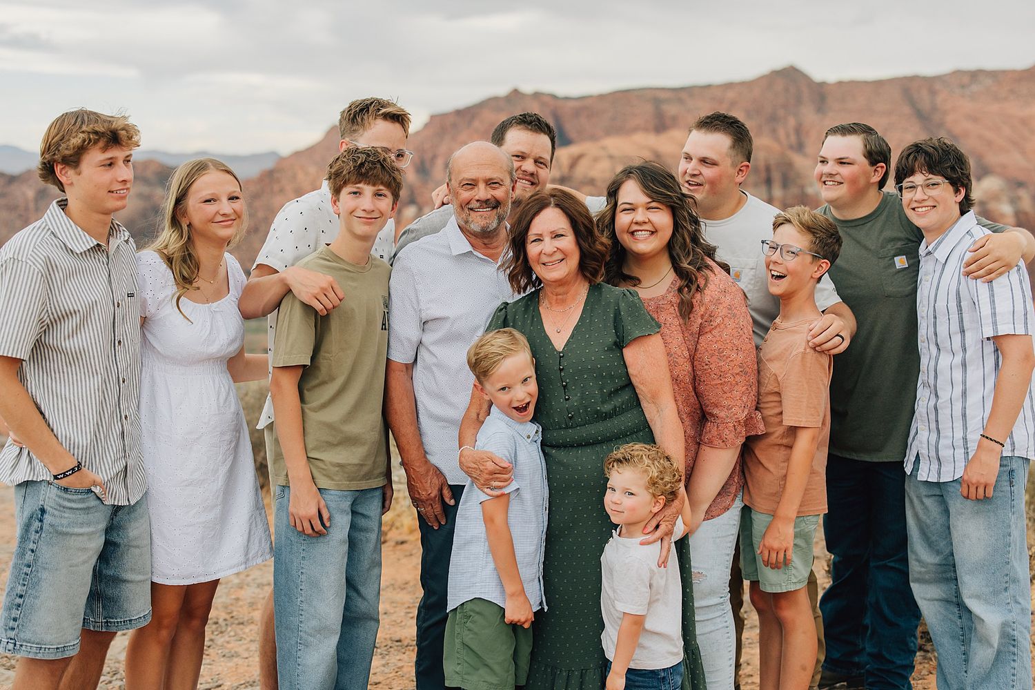 Large family group portrait smiling outdoors with red rock canyon landscape in background.