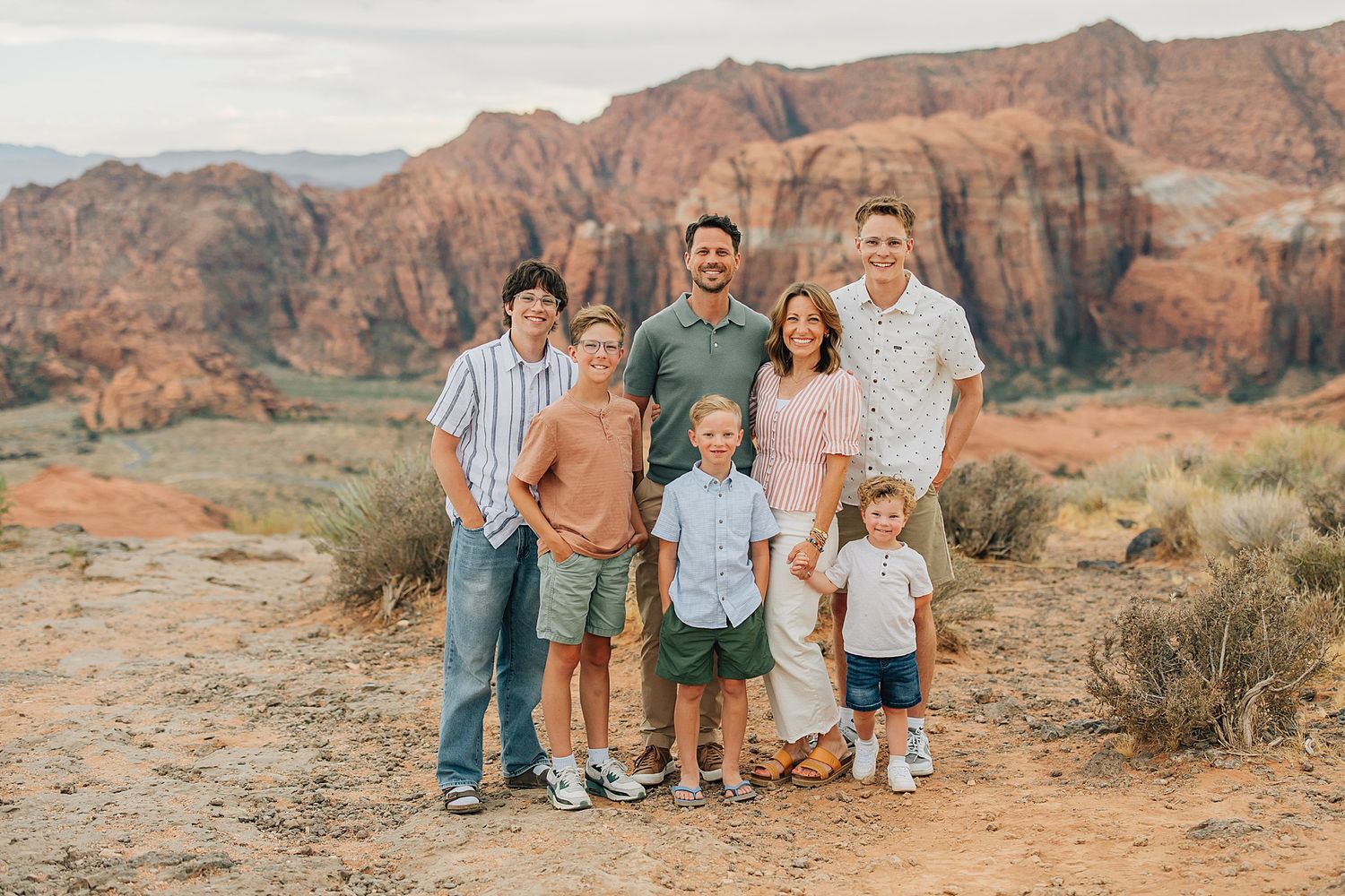 Family of seven posing together outdoors with stunning red rock canyon formations in the background.