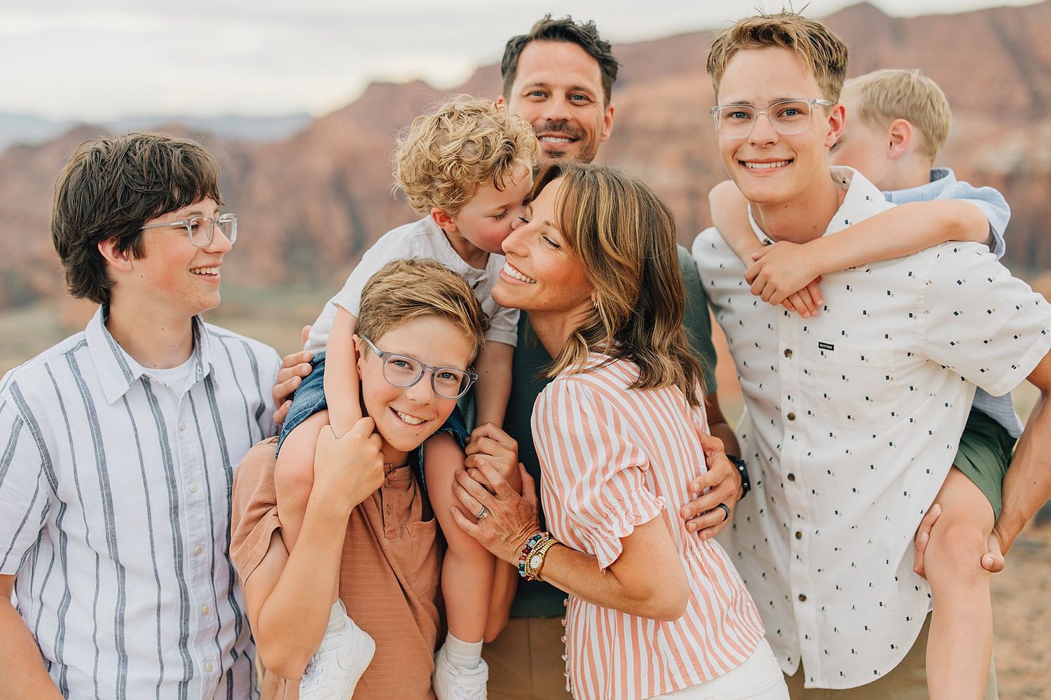 Happy family of six smiling and embracing outdoors with red rock formations in the background.