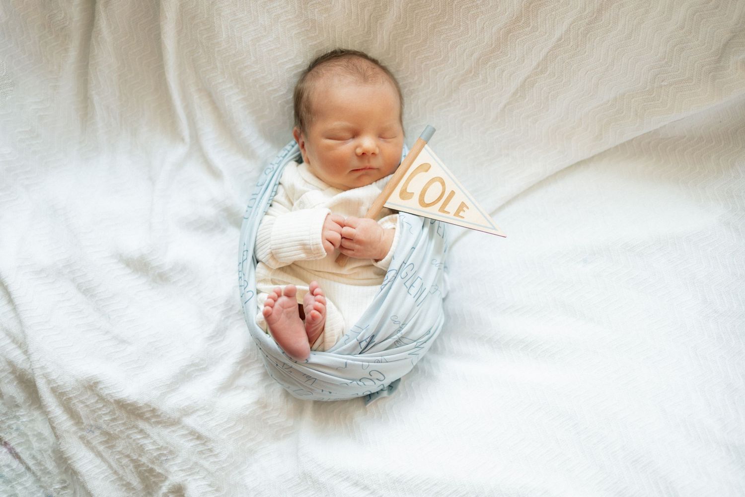Newborn baby wrapped in blue swaddle sleeping peacefully on white blanket at University of Tennessee Medical Center.