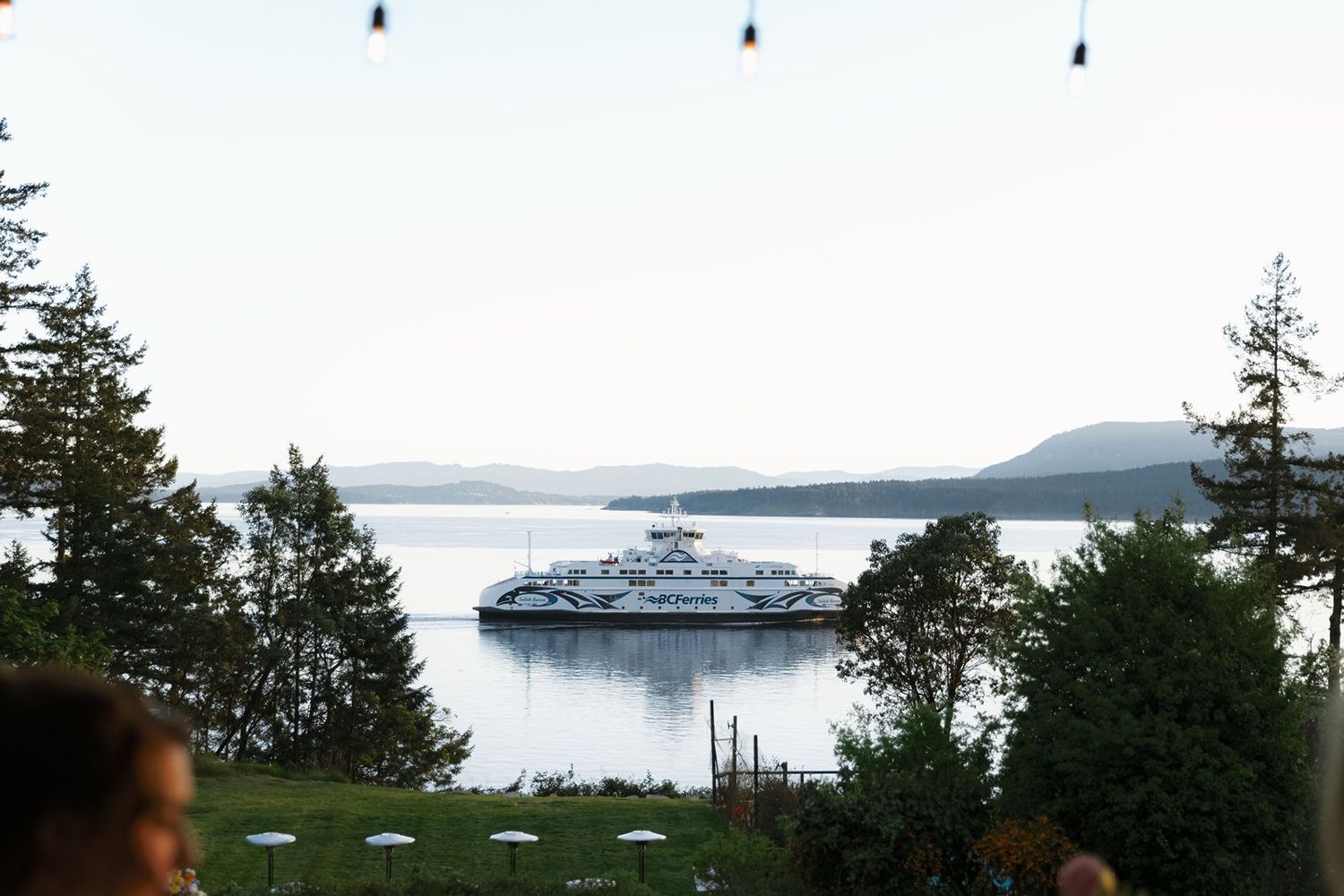 A Washington State Ferry glides across calm waters near San Juan Islands, viewed from a scenic waterfront venue at dusk.