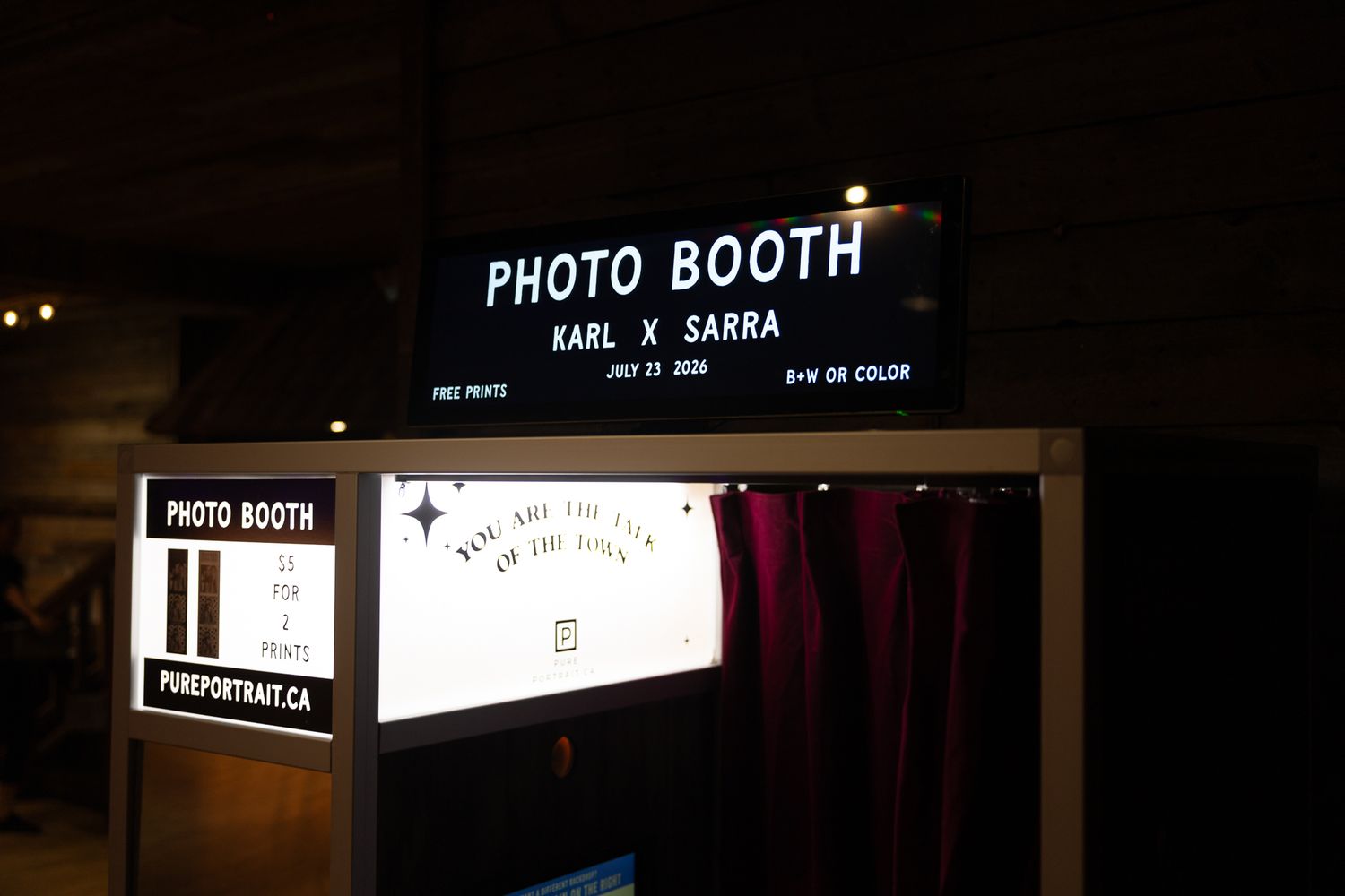 Vintage photo booth with red curtain, cow print walls, checkered floor, and chrome stool offering black & white or color photo strips.