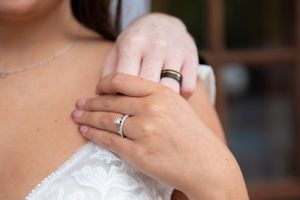 Close-up of bride and groom hands on her shoulder displaying their matching wedding bands.