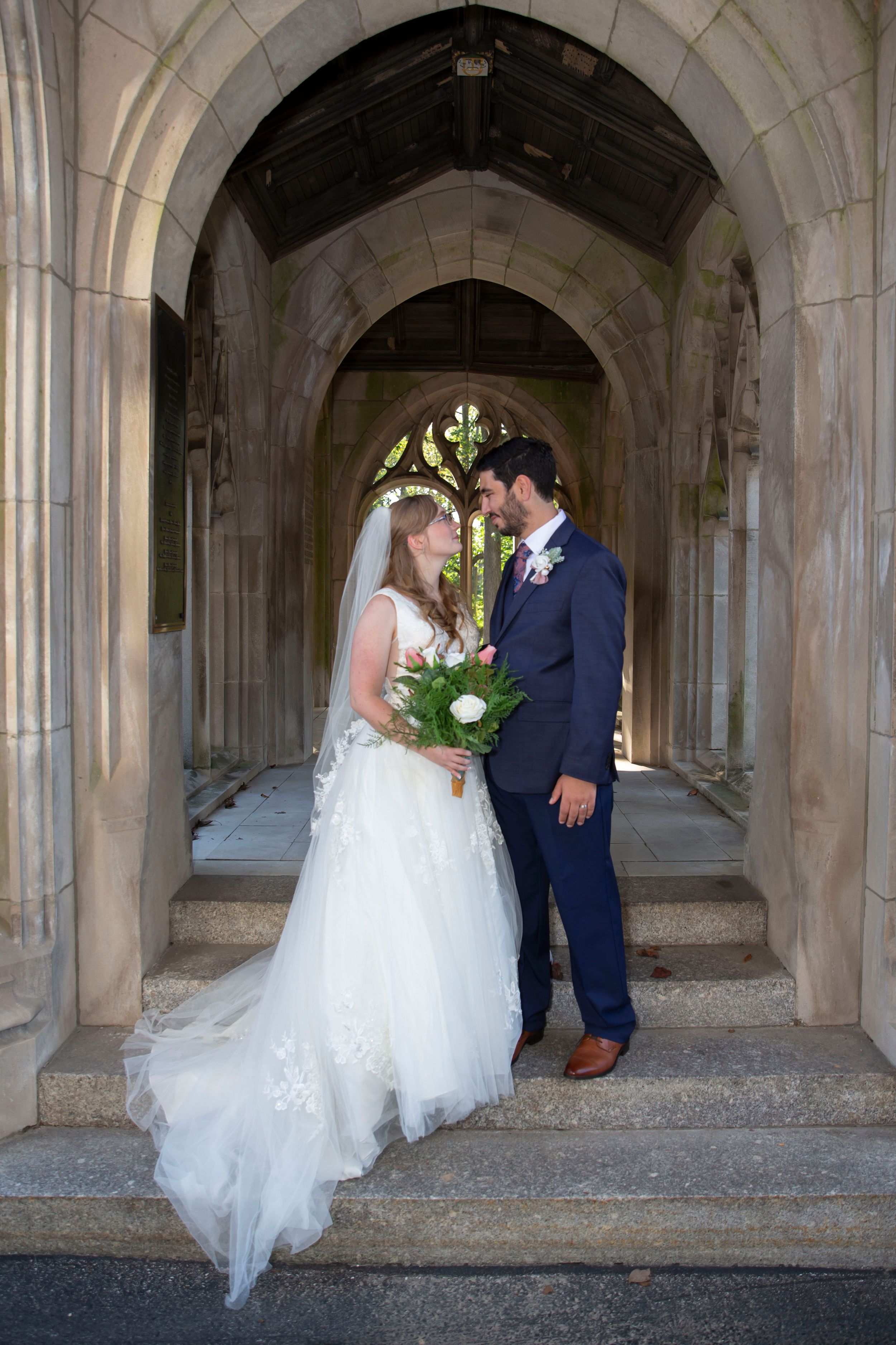 Bride and groom share a romantic moment under a Gothic stone arch at their wedding venue.