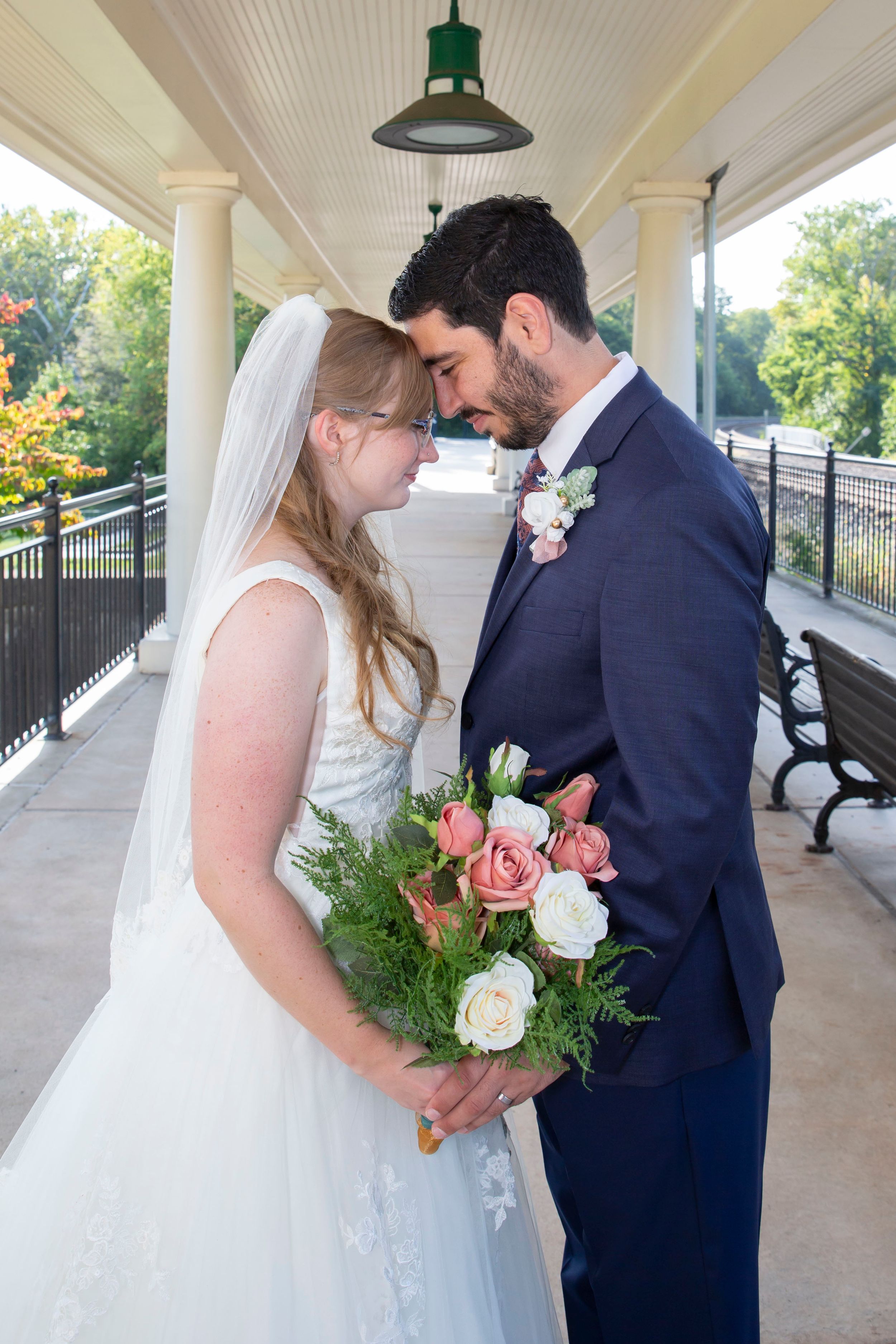 Bride and groom share an intimate forehead touch moment on a covered outdoor wedding venue porch.