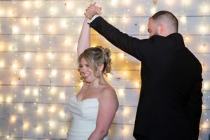 Bride and groom share first dance in front of a sparkling fairy light wall at their wedding reception.